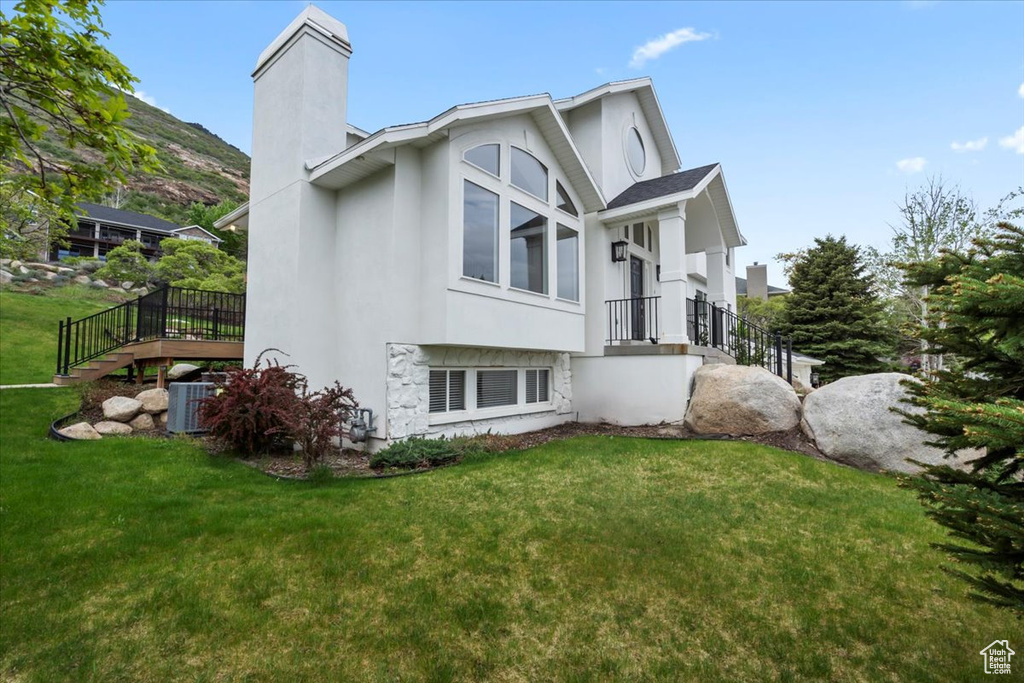 View of side of property with central air condition unit, stucco siding, a chimney, and a lawn