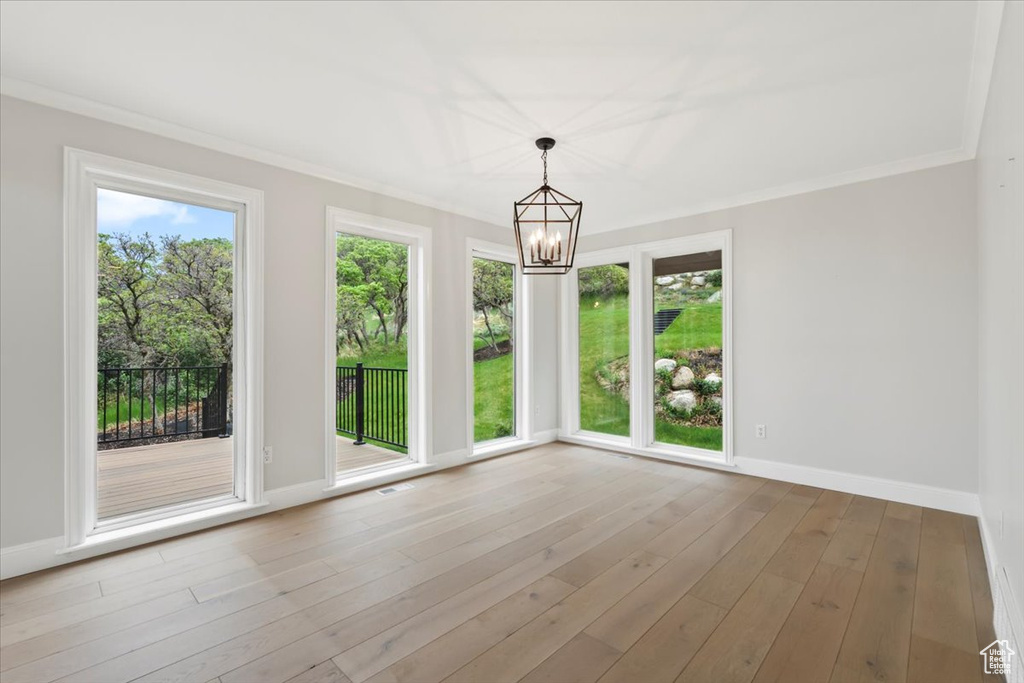Unfurnished dining area with crown molding, a notable chandelier, baseboards, and wood finished floors