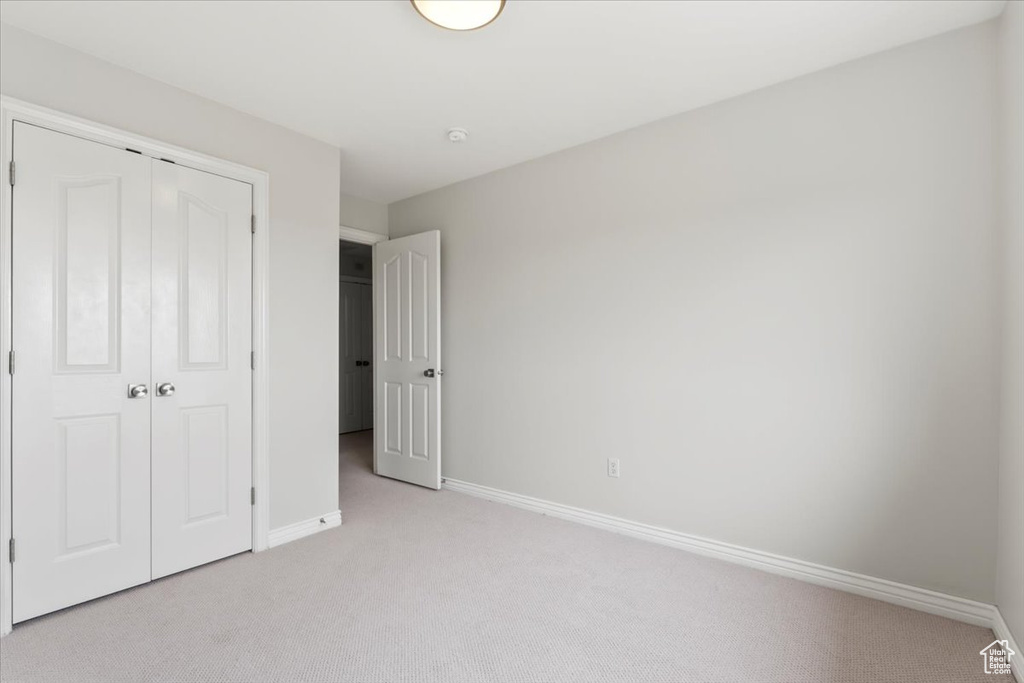Unfurnished bedroom featuring baseboards, light carpet, and a closet