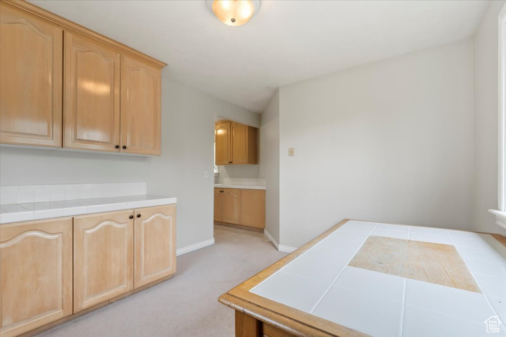 Kitchen with light colored carpet, tile countertops, light brown cabinetry, and baseboards