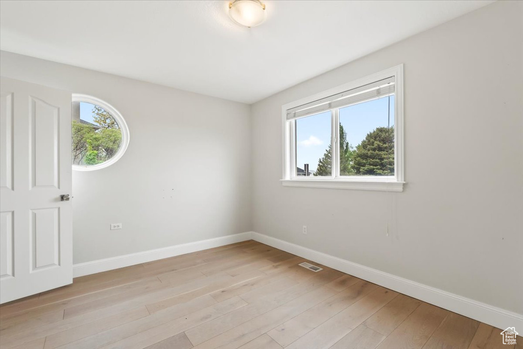 Empty room with light wood-type flooring, visible vents, and baseboards