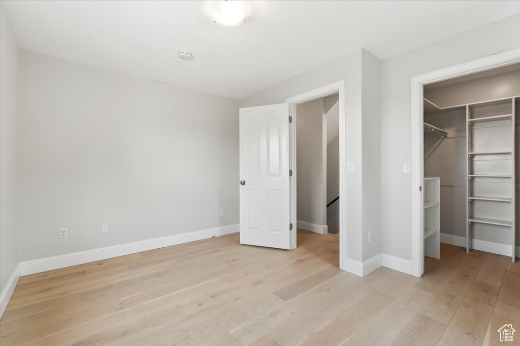 Unfurnished bedroom featuring light wood-style flooring, a spacious closet, baseboards, and a closet