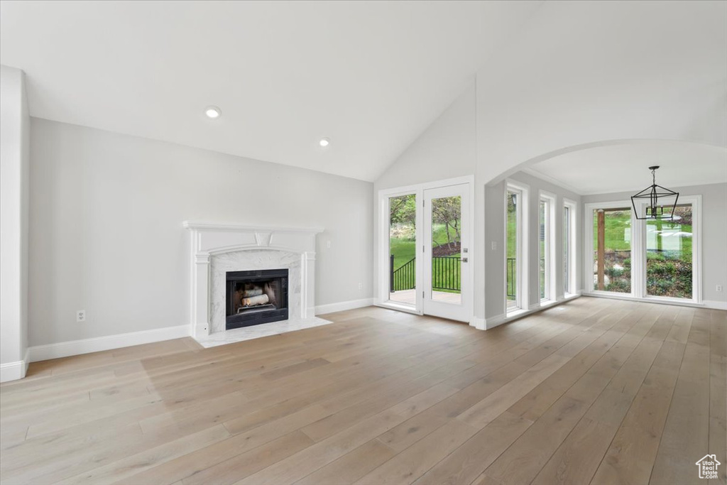 Unfurnished living room with light wood-style flooring, a premium fireplace, a notable chandelier, baseboards, and arched walkways