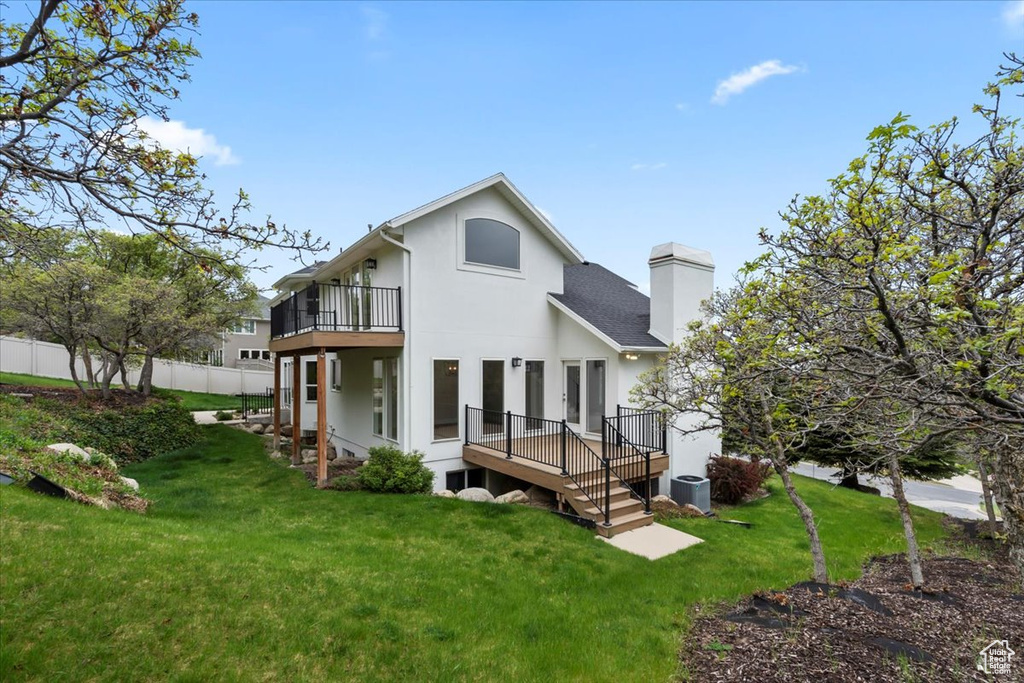 Rear view of property with a balcony, a chimney, a lawn, fence, and central AC unit