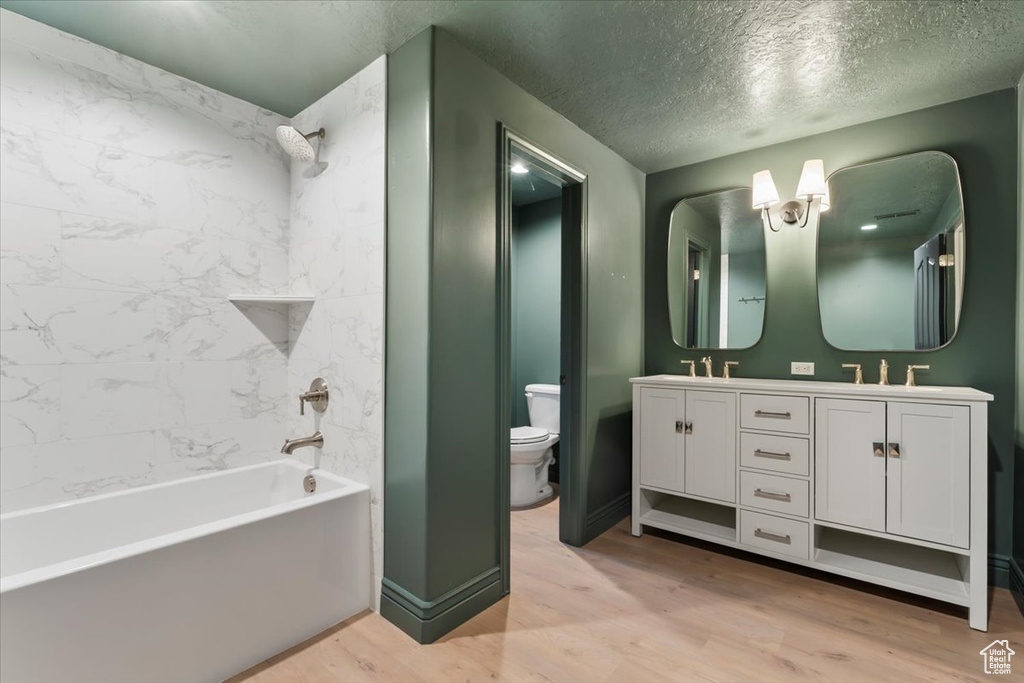 Full bath with double vanity, toilet, a textured ceiling, and wood finished floors