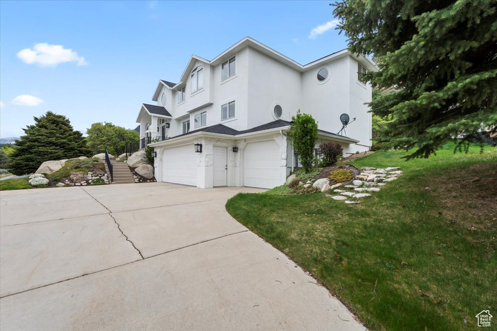 View of side of home featuring a lawn, driveway, a garage, stucco siding, and stairway