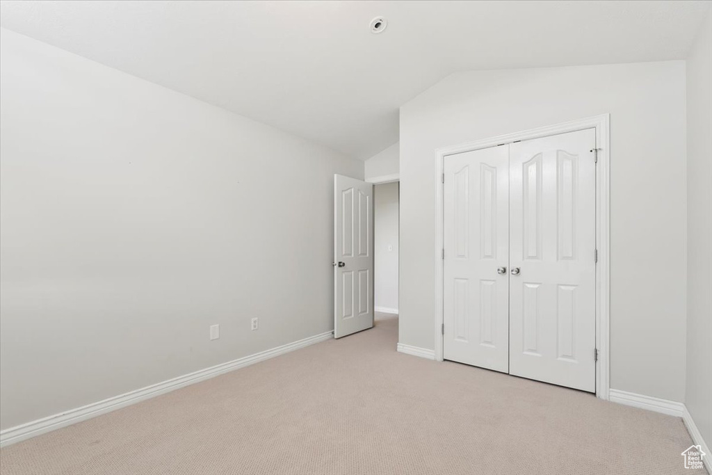 Unfurnished bedroom featuring light colored carpet, a closet, baseboards, and lofted ceiling