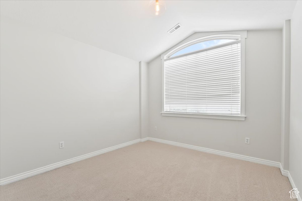 Unfurnished room featuring plenty of natural light, vaulted ceiling, visible vents, and light carpet