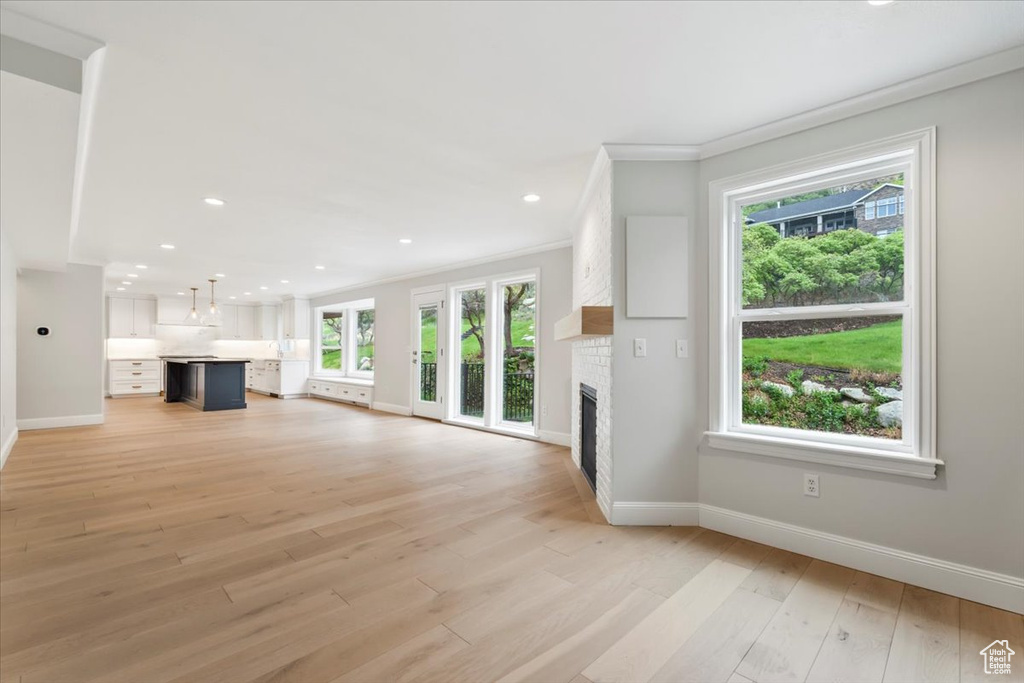 Unfurnished living room with recessed lighting, crown molding, a brick fireplace, baseboards, and light wood-style floors
