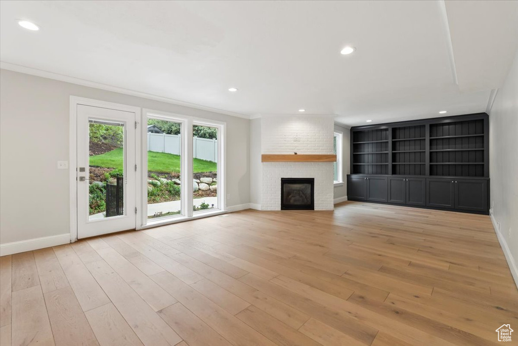Unfurnished living room with a fireplace, crown molding, light wood-type flooring, baseboards, and recessed lighting