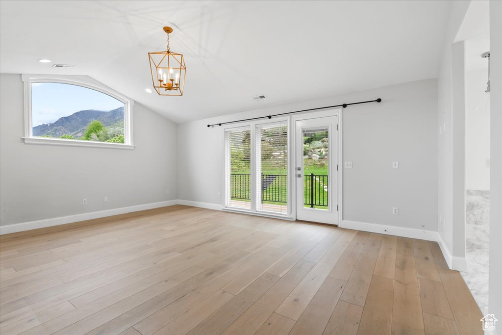 Spare room with baseboards, an inviting chandelier, light wood-type flooring, and plenty of natural light