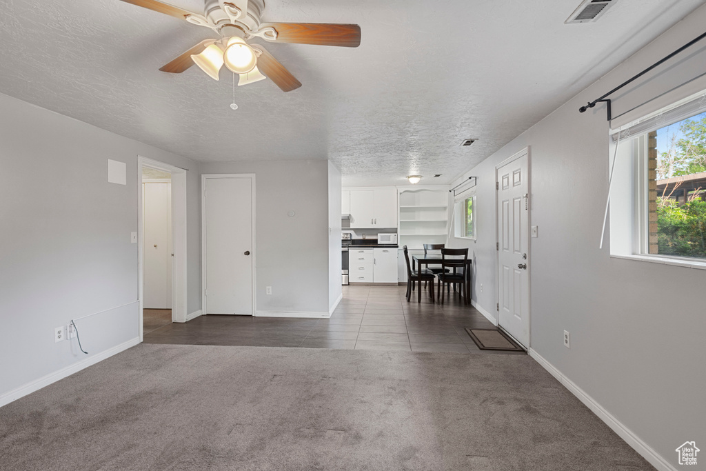 Living room featuring ceiling fan, a textured ceiling, visible vents, baseboards, and dark carpet