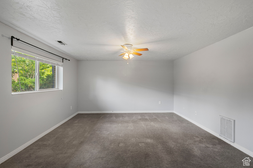 Carpeted empty room with visible vents, a ceiling fan, and a textured ceiling