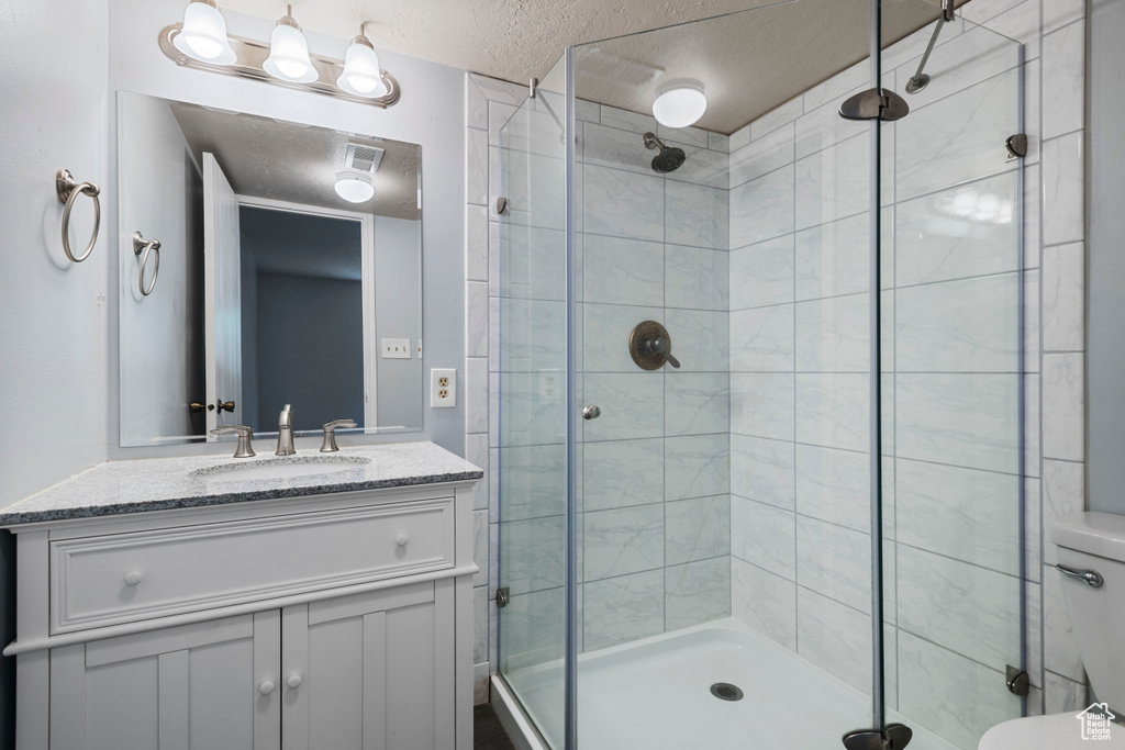 Bathroom featuring vanity, visible vents, toilet, a textured ceiling, and a stall shower