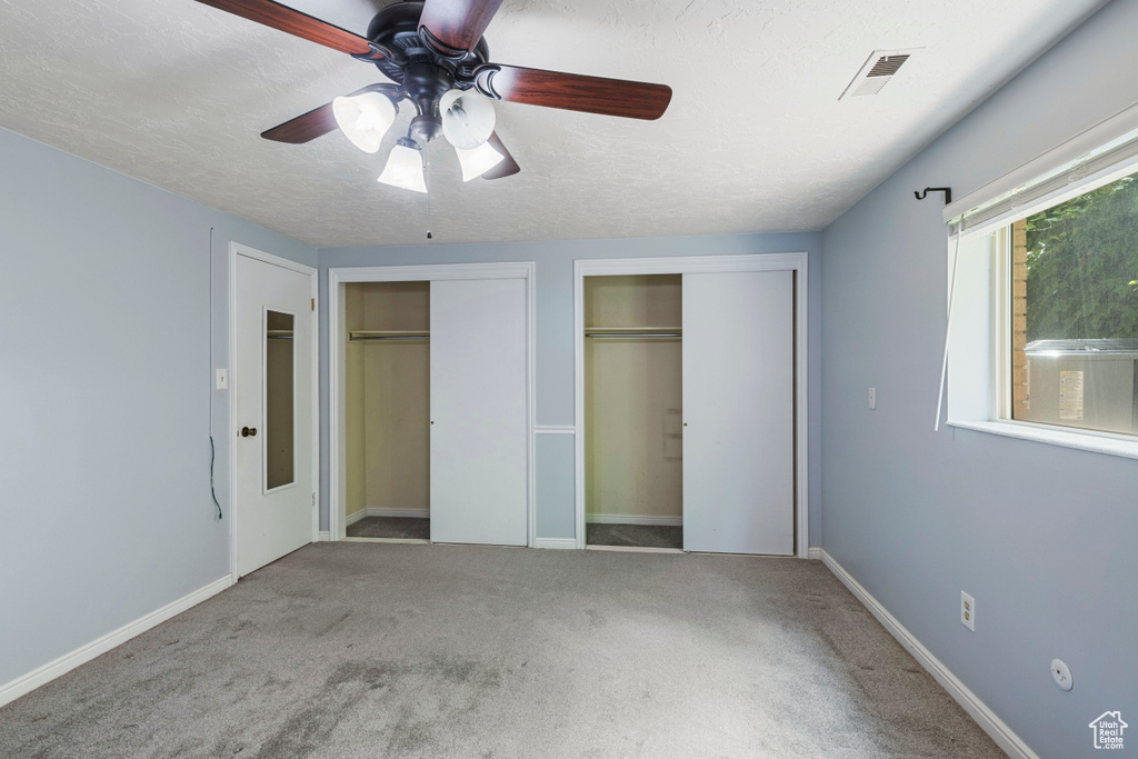 Unfurnished bedroom featuring two closets, a textured ceiling, visible vents, and carpet floors
