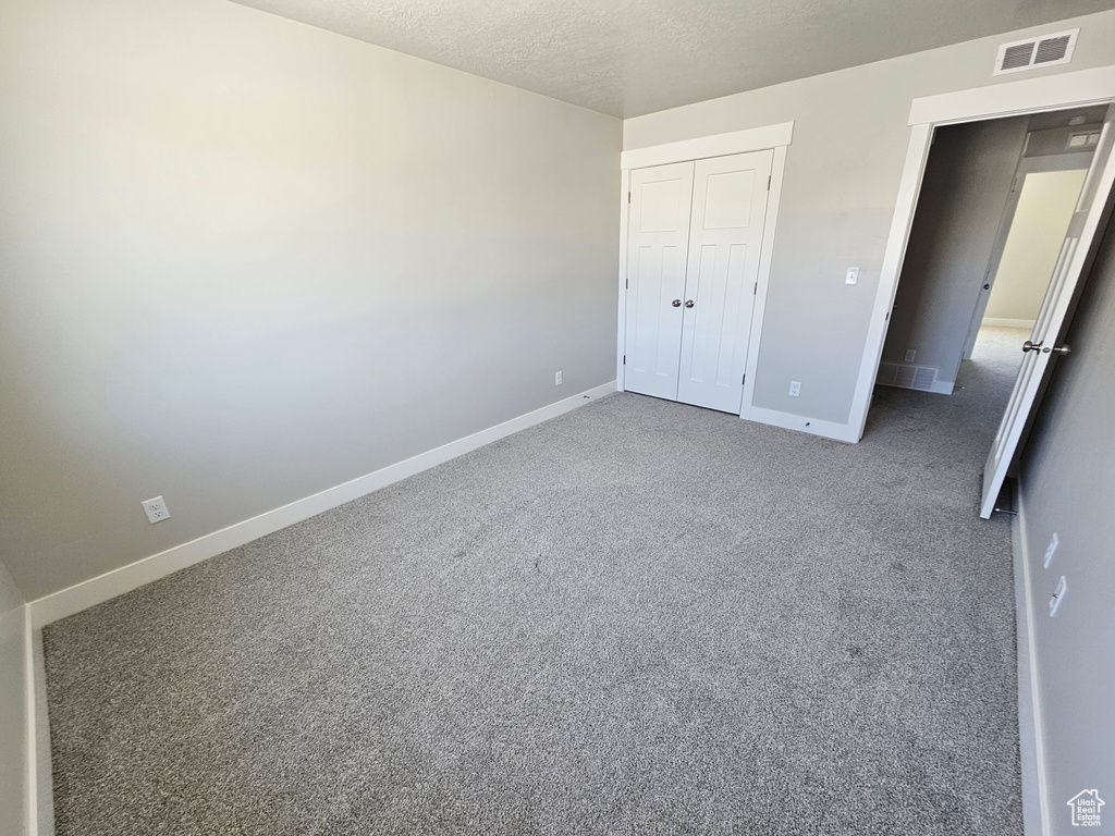 Unfurnished bedroom with a textured ceiling, baseboards, visible vents, a closet, and carpet floors