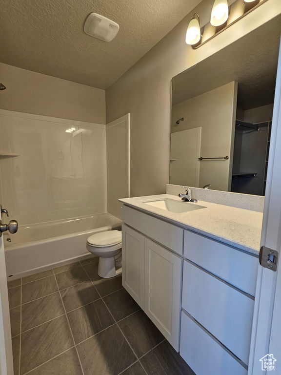 Full bath with tile patterned floors, a textured ceiling, shower / bathing tub combination, vanity, and toilet