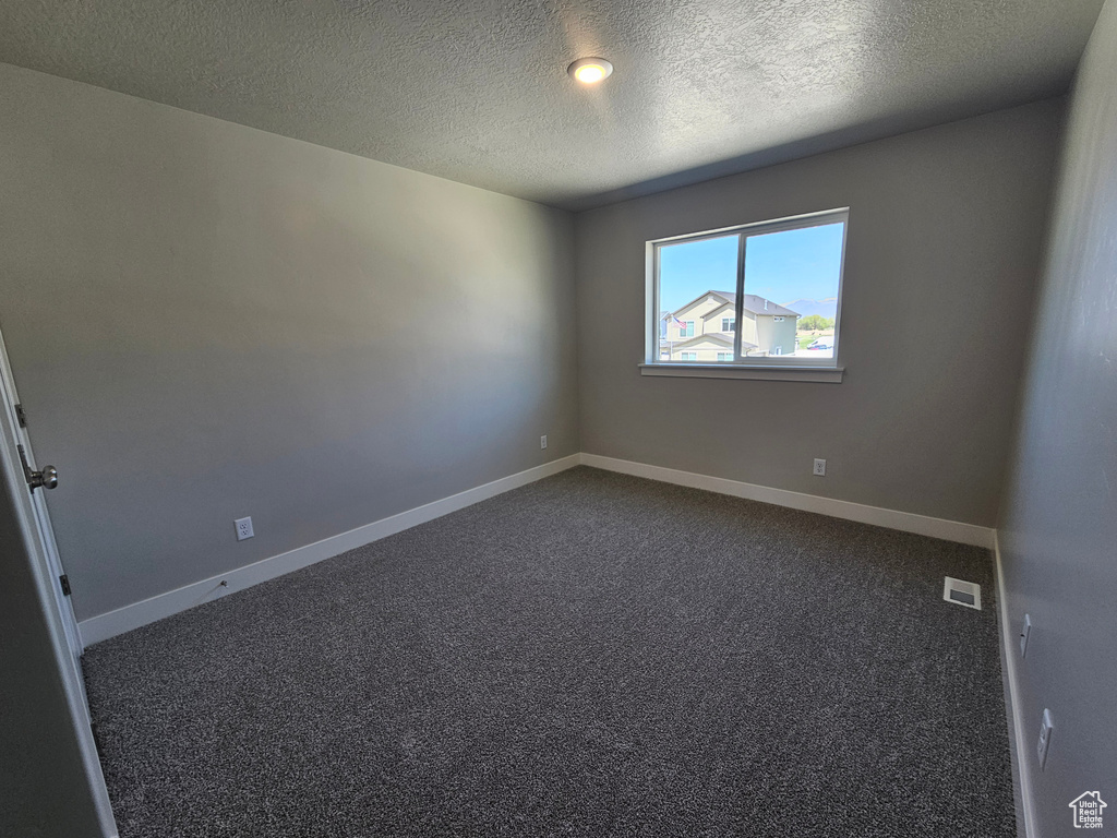 Empty room featuring dark carpet, baseboards, visible vents, and a textured ceiling