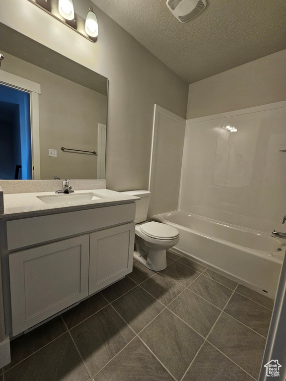 Bathroom featuring tile patterned floors, toilet, vanity,  shower combination, and a textured ceiling