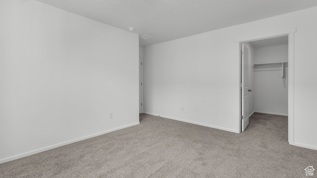 Unfurnished bedroom with a walk in closet, baseboards, and carpet