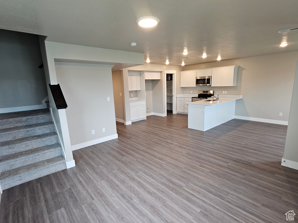 Kitchen featuring appliances with stainless steel finishes, dark wood finished floors, baseboards, white cabinets, and a peninsula