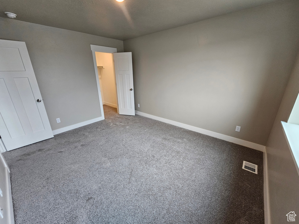 Unfurnished bedroom with a walk in closet, visible vents, baseboards, a closet, and carpet