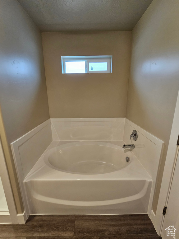 Bathroom with a garden tub, a textured ceiling, and wood finished floors