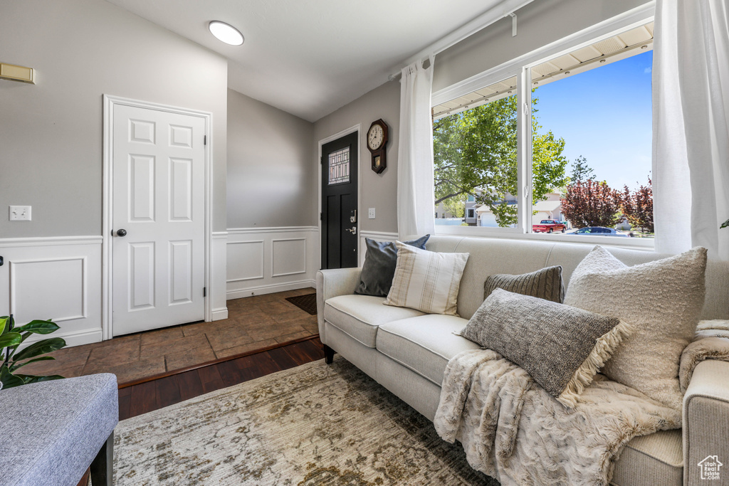 Living area with vaulted ceiling, a decorative wall, wainscoting, and wood finished floors