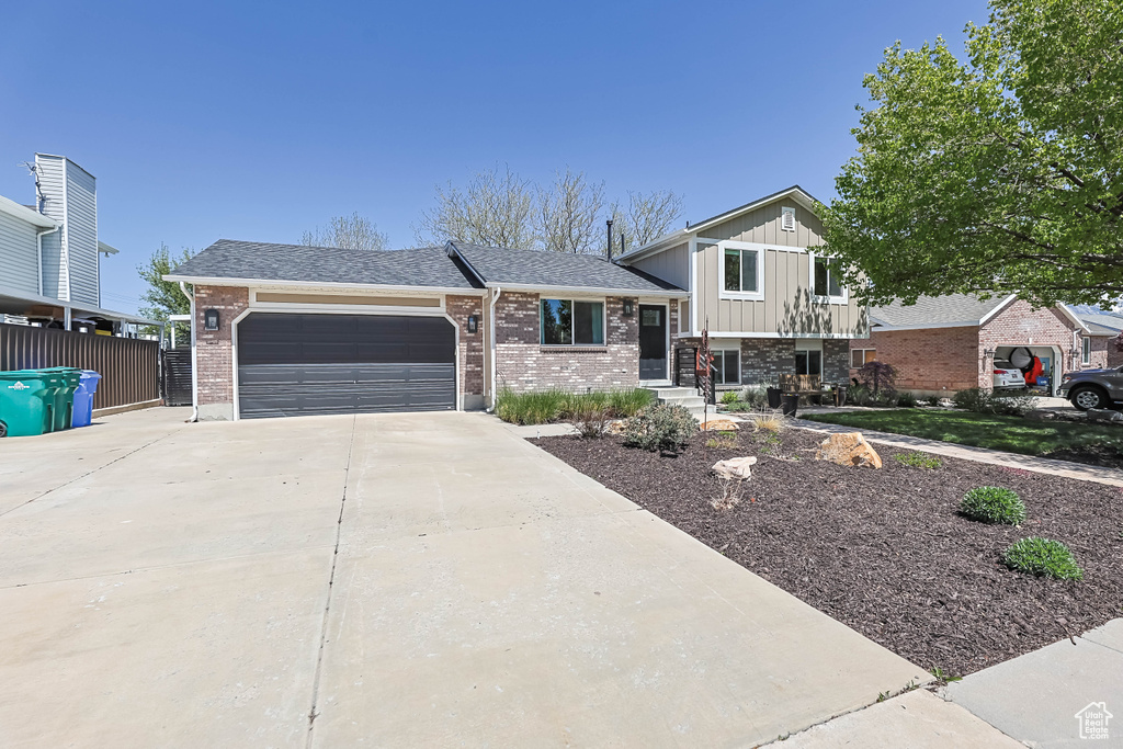Split level home featuring board and batten siding, a garage, brick siding, fence, and concrete driveway