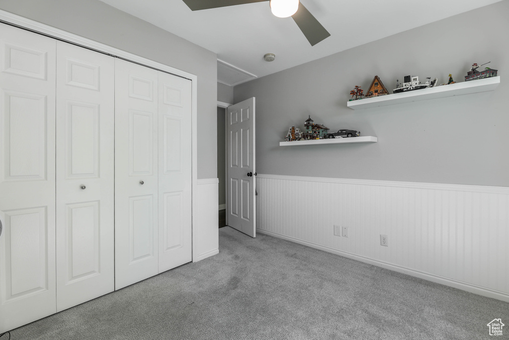 Unfurnished bedroom featuring carpet floors, a closet, a ceiling fan, and a wainscoted wall