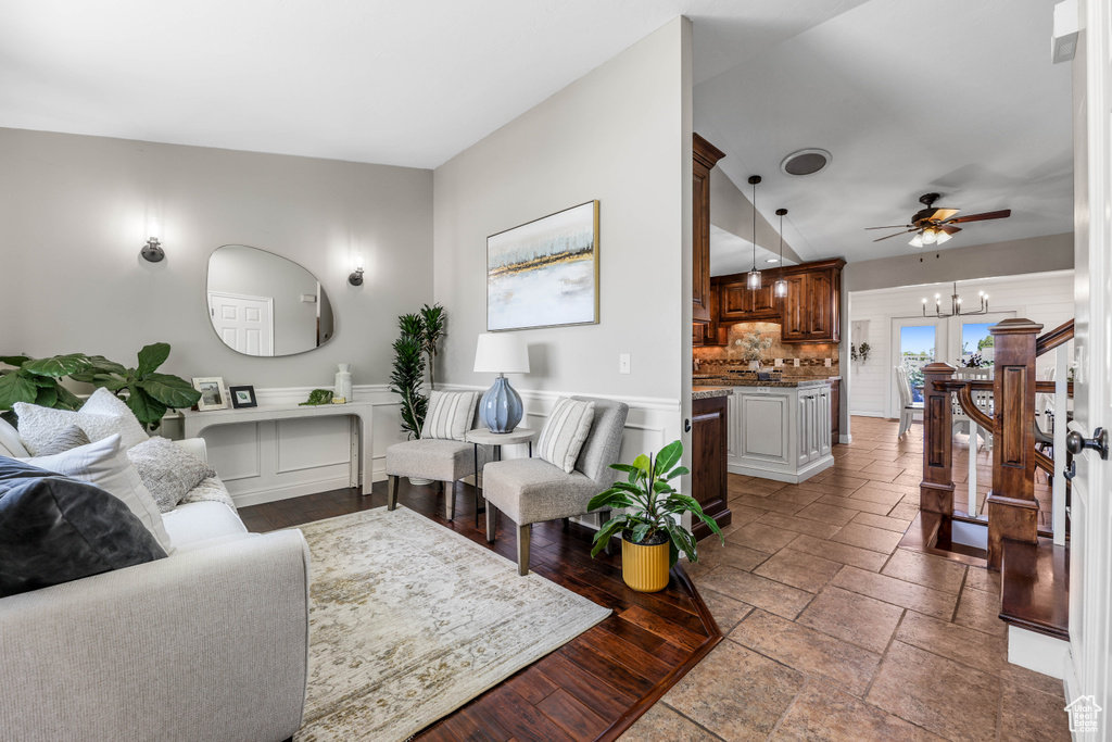Living area featuring stone tile flooring, a ceiling fan, and a wainscoted wall