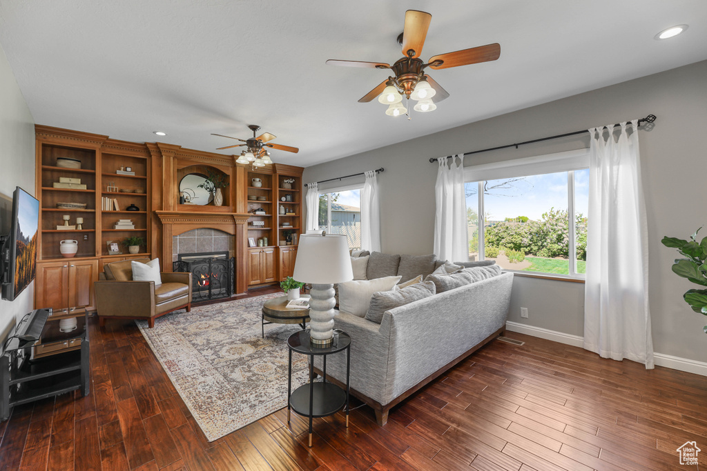 Living area with dark wood-style flooring, baseboards, ceiling fan, recessed lighting, and a tiled fireplace