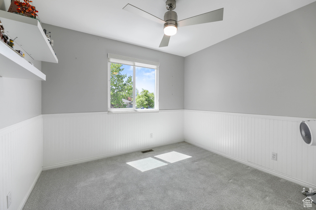 Carpeted empty room featuring a ceiling fan, visible vents, and wainscoting