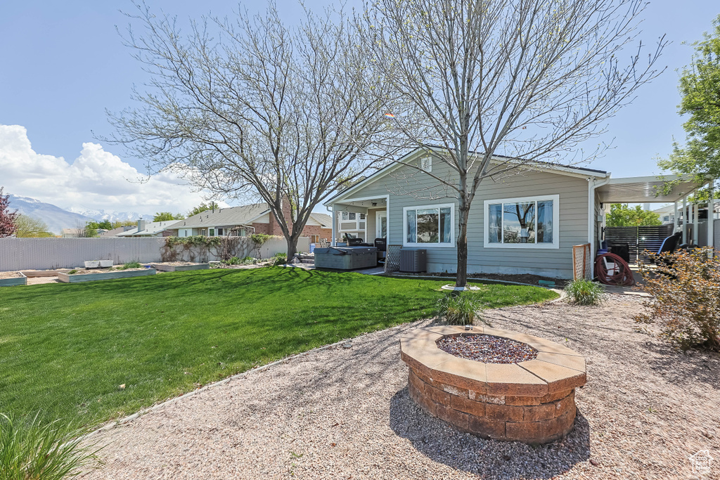 Back of house with a fenced backyard, a hot tub, central AC, and a fire pit
