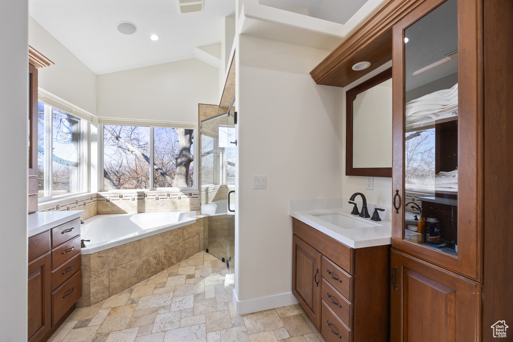 Bathroom with stone tile flooring, a garden tub, vanity, baseboards, and a shower stall
