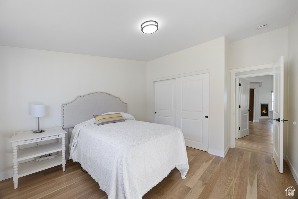 Bedroom with a closet, baseboards, a lit fireplace, and light wood-type flooring