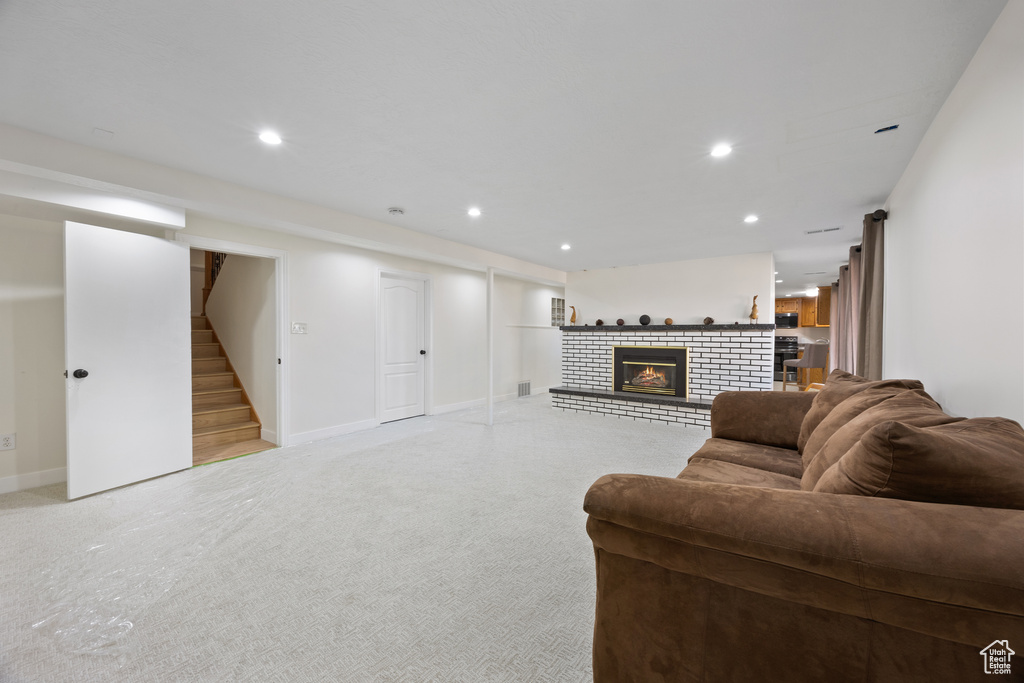 Living room with a brick fireplace, recessed lighting, light colored carpet, and stairway