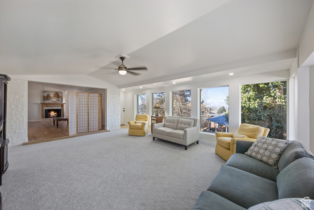 Living area featuring carpet floors, a ceiling fan, lofted ceiling, and a warm lit fireplace