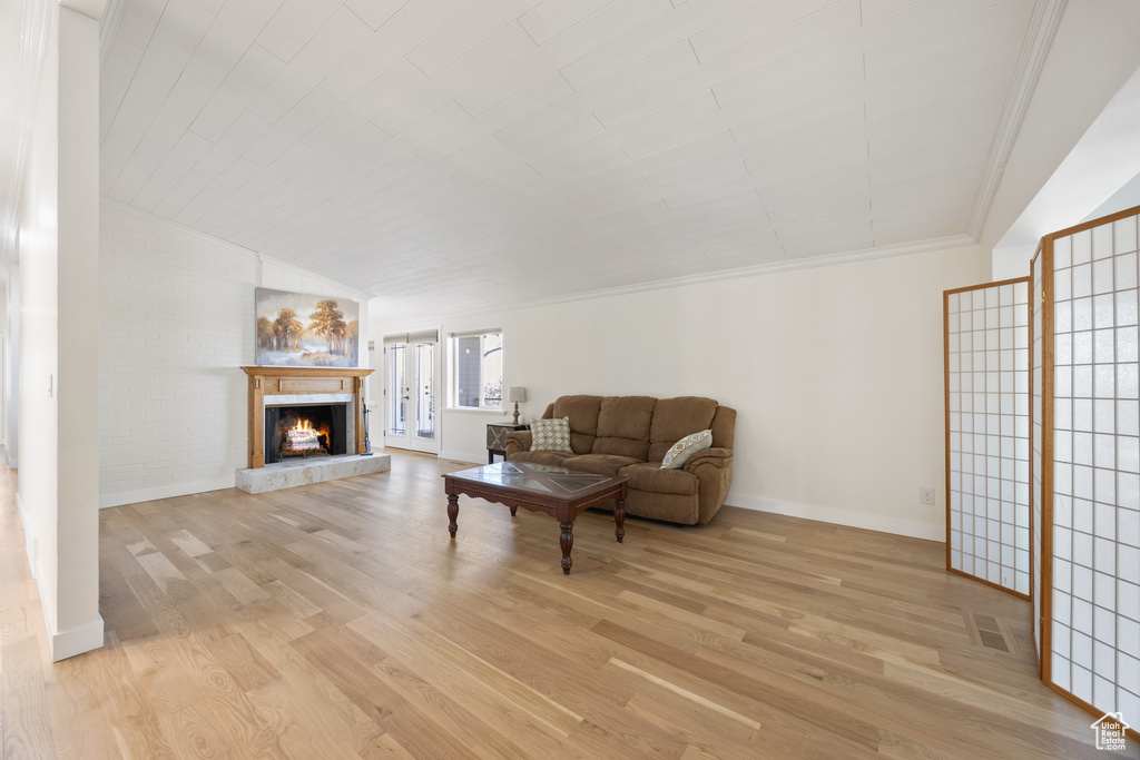 Living area featuring baseboards, a warm lit fireplace, crown molding, and light wood-style flooring