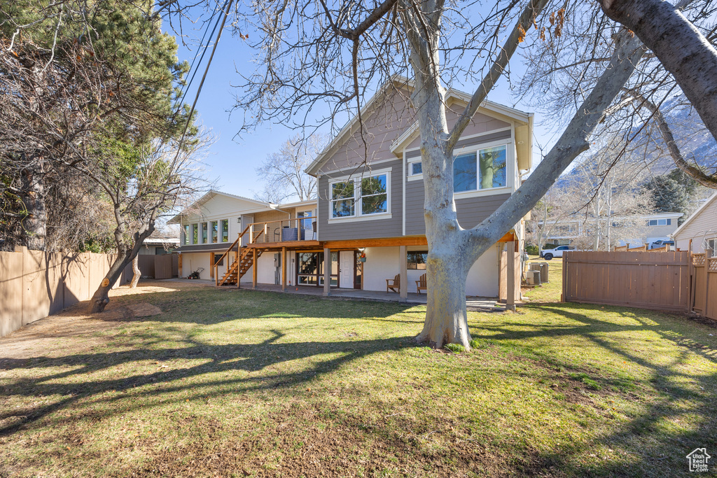 Rear view of property with a lawn, a fenced backyard, a wooden deck, and stairway