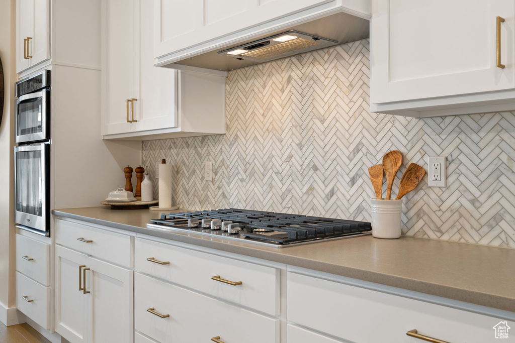 Kitchen featuring stainless steel appliances, tasteful backsplash, custom exhaust hood, light countertops, and white cabinets