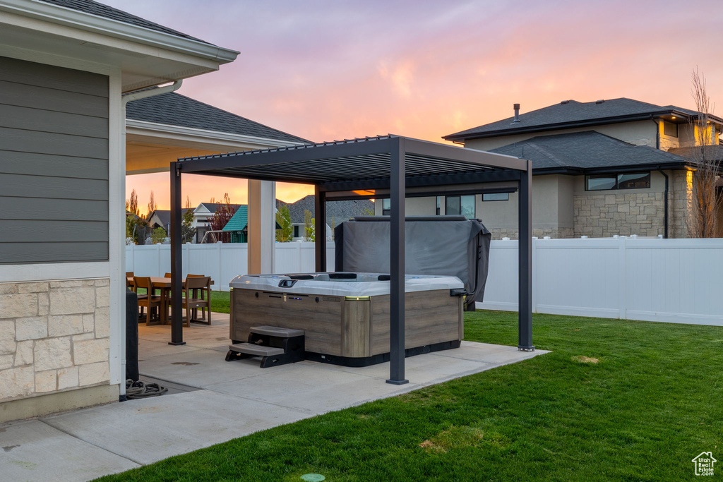 Patio terrace at dusk with outdoor dining area, a hot tub, a pergola, a lawn, and a fenced backyard