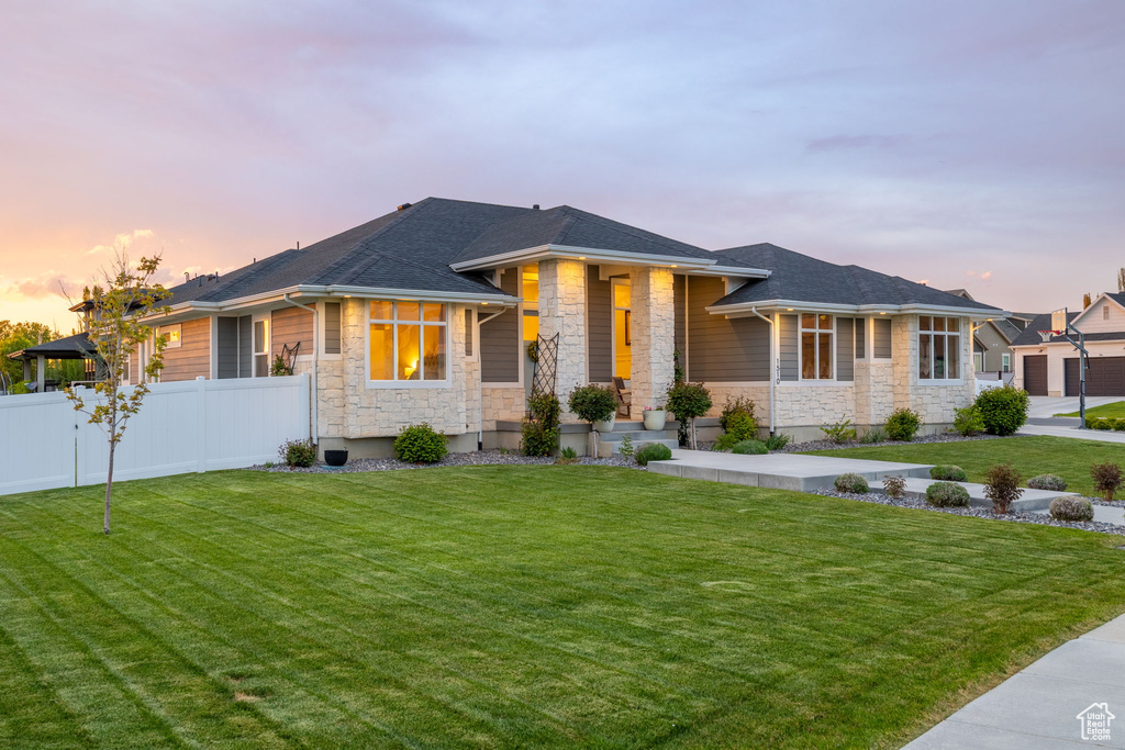 Prairie-style house featuring fence, a shingled roof, a front yard, and stone siding