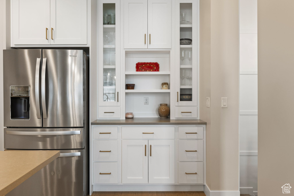 Kitchen featuring glass insert cabinets, stainless steel fridge, white cabinetry, and baseboards