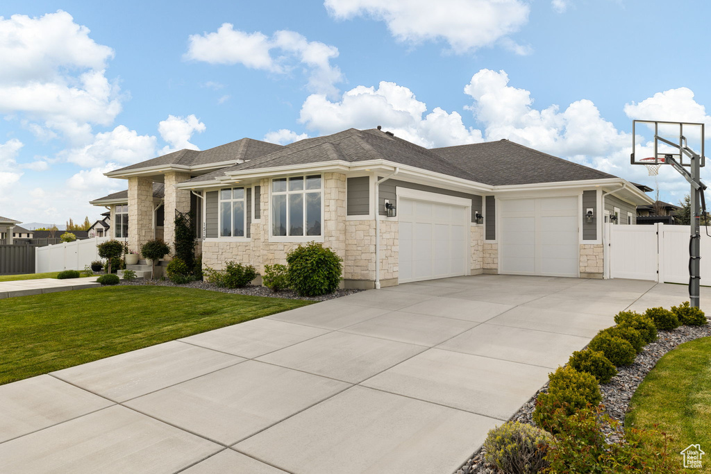 View of front of property with a front lawn, a garage, a gate, stone siding, and fence