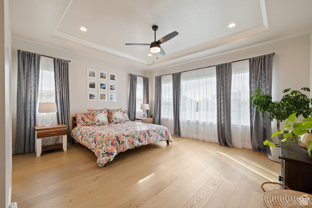 Bedroom featuring light wood-type flooring, recessed lighting, multiple windows, and a tray ceiling