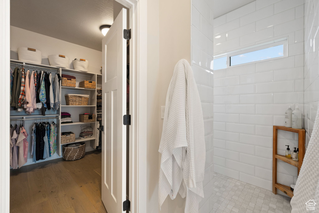Bathroom with a spacious closet, wood finished floors, and a tile shower