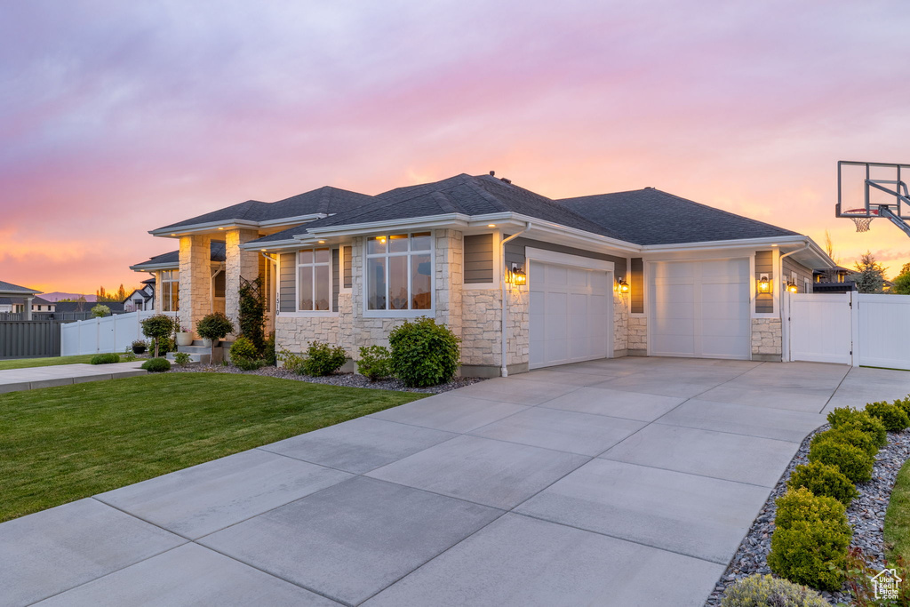 Prairie-style home featuring a yard, a gate, fence, stone siding, and an attached garage