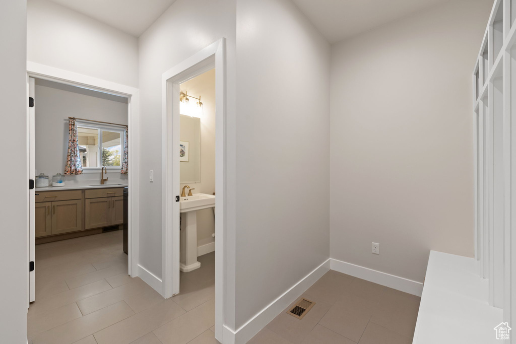 Corridor featuring light tile patterned floors, visible vents, baseboards, and a sink