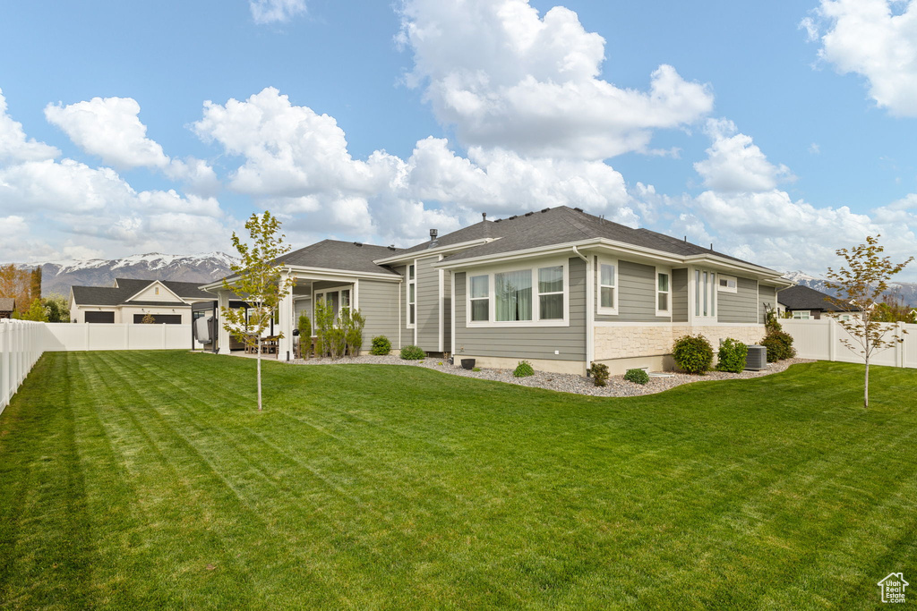Rear view of property with a lawn, stone siding, central AC, and a fenced backyard